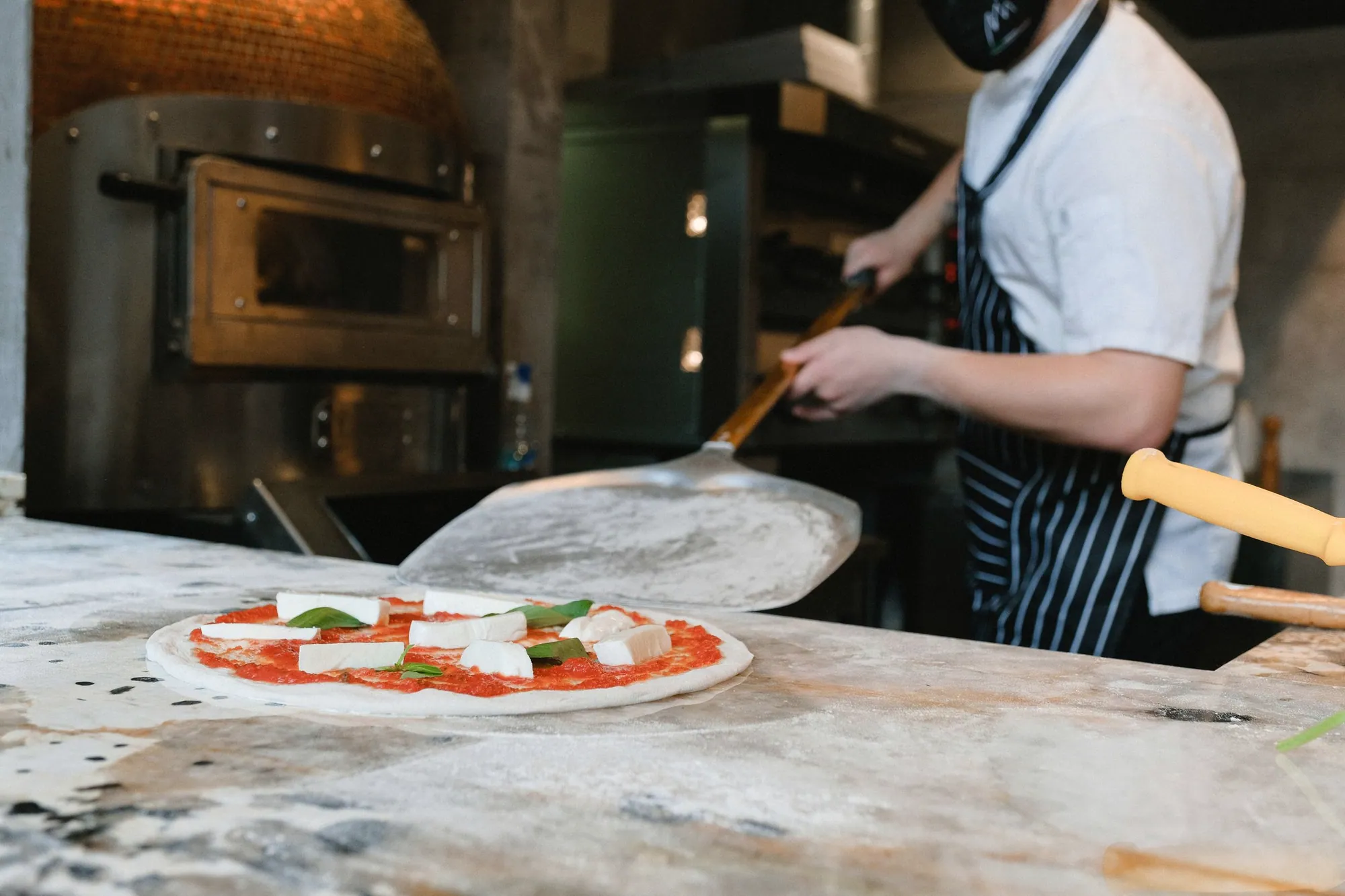 Chef sliding a pizza into a traditional oven in a pizzeria kitchen